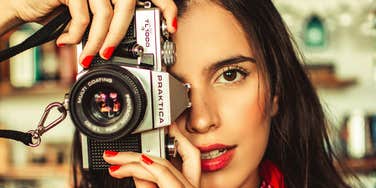 Woman holding a vintage film camera close to her face indoors.