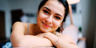 A woman resting her arms on a couch, smiling gently in a calm indoor setting.