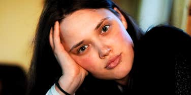 A woman with dark hair resting her head on her hand inside a room.