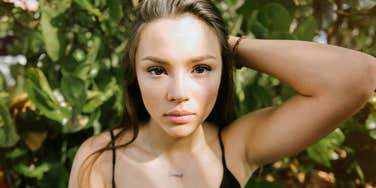 A woman standing outdoors with a serious, reflective expression, conveying emotional complexity and introspection.