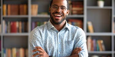 creative man standing in front of book shelf smiling