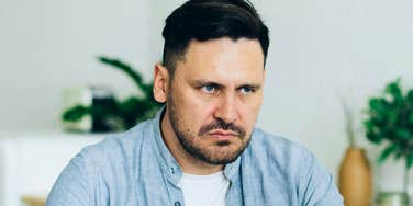 Serious-looking man sitting indoors with a tense expression