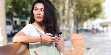Fearful mom sitting on a bench and scrolling her phone 