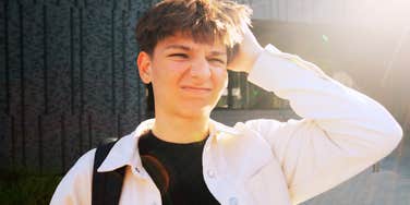 A preteen boy outdoors squinting, wearing a light jacket and backpack.