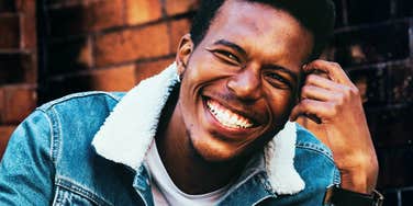 Man smiling outdoors near a brick wall.