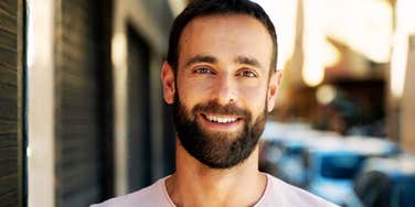 Smiling bearded man standing outdoors on a city street.