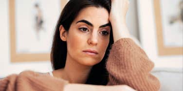 A woman rests her head on her hand while sitting indoors, looking thoughtful.
