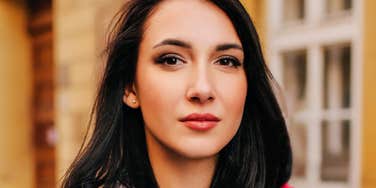 A close-up portrait of a woman standing outdoors in warm natural light.