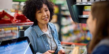 woman who refuses to use the self-checkout talking to cashier at grocery store