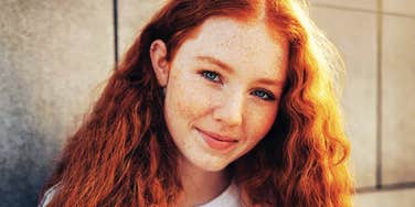 A close-up portrait of a woman with long red hair and freckles.