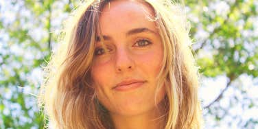 A woman with blonde hair looking directly at the camera outdoors in sunlight.