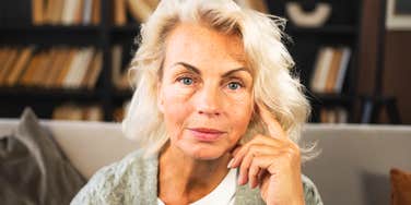 An older woman with white hair sitting indoors and looking at the camera.