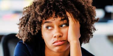 A woman with curly hair resting her head on her hand and looking off to the side.