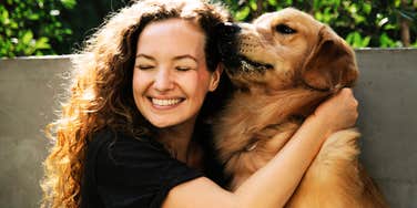 A woman hugging a dog outdoors.