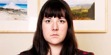A woman looking straight at the camera while sitting indoors.