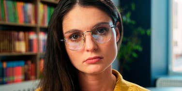 A woman wearing glasses looking directly at the camera indoors.