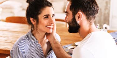 A couple smiling at each other while sitting at a table indoors.