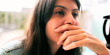 A woman resting her hand near her face while looking off to the side indoors.