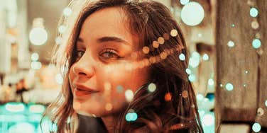 Woman looking over her shoulder with city lights blurred in the background.