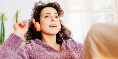 Woman wearing headphones and relaxing indoors near a window.