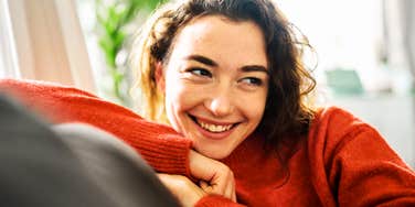 A woman smiling while leaning forward indoors.