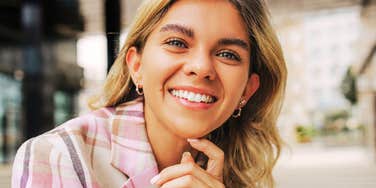 A woman smiling confidently while leaning forward outdoors.