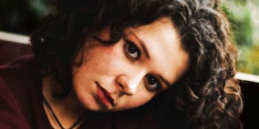 Close-up portrait of a woman with curly hair looking at the camera in soft natural light.