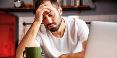 Exhausted man with his hand on his head near laptop.