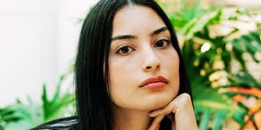 A woman with dark hair looking directly at the camera while resting her chin on her hand.