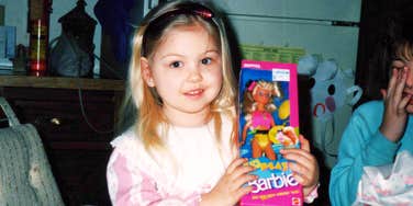 A young child holding a boxed fashion doll during a 1990s holiday celebration.