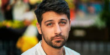 A man with a controlled, appraising expression making direct eye contact, appearing quietly judgmental