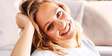 A woman smiling while resting her head on her hand indoors.