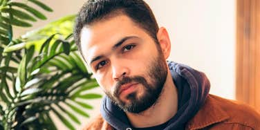 A thoughtful man looking at his phone indoors, appearing uncertain, reflecting modern texting habits that can unintentionally stall conversations.