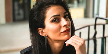 A woman with dark hair resting her chin on her hand outdoors.