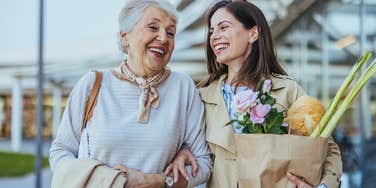 two happy women walking with bag of groceries