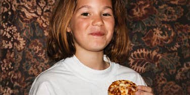 A child holding a small snack and smiling at the camera indoors