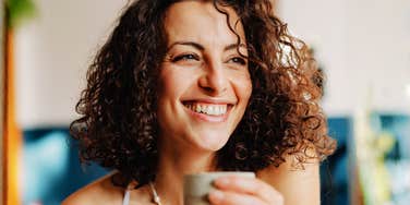 Smiling person with curly hair holding a mug indoors