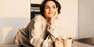 woman in cozy sweater holding a coffee mug at kitchen counter in warm morning light