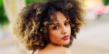 thoughtful woman looking over her shoulder with reflective expression in soft outdoor light, subtle emotional depth conveying post-divorce self-reflection and healing journey