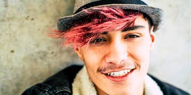 Gen Z young man with pink bangs and old-fashioned hat smiling
