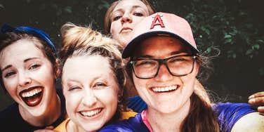 close-up group selfie of four joyful women smiling and laughing together outdoors