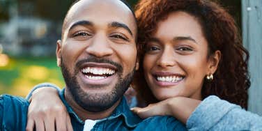 Two people smiling together outdoors with their arms around each other