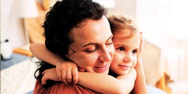 parent hugging young child tightly at home, both with eyes closed and soft smiles in a warm, affectionate moment