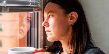 Woman holding a mug and looking out a window.