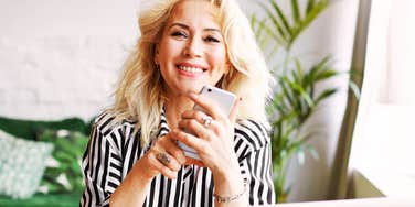 confident midlife professional smiling while holding smartphone at home office desk.