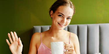 woman in pink tank top holding coffee mug and smiling in a calm, minimalist bedroom, fresh start energy and peaceful morning routine reflecting the mental clarity that comes from declutterin