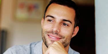 Man smiling while resting his chin on his hand indoors