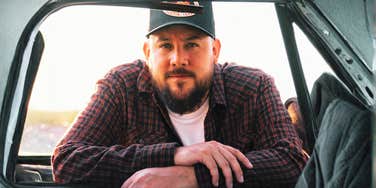 Man leaning against a door window with a serious, distant expression, conveying introspection and emotional withdrawal.