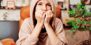 person wearing a hooded sweater sitting indoors with hands near their face