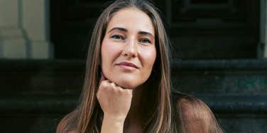 Person with long hair sitting on steps and looking at the camera.